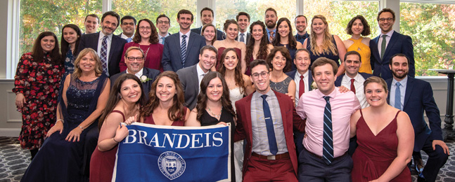 Large group of people posed behind an upheld Brandeis banner